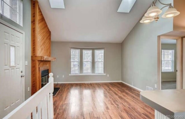 unfurnished living room with baseboards, a glass covered fireplace, wood finished floors, and vaulted ceiling with skylight