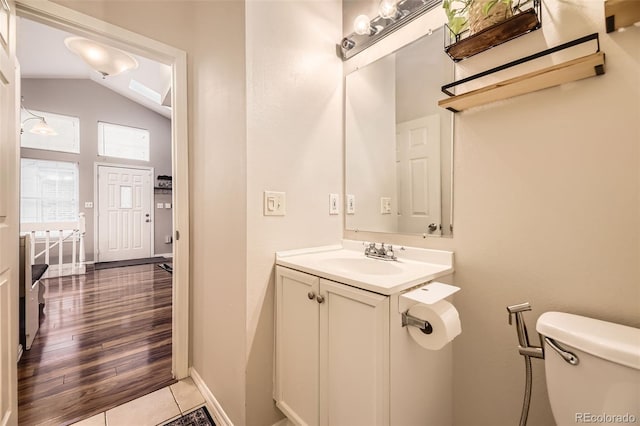 half bathroom with toilet, baseboards, lofted ceiling, and vanity