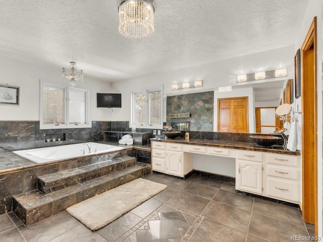 bathroom with tiled tub, vanity, a notable chandelier, and a textured ceiling