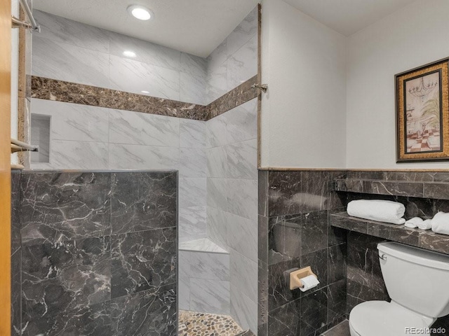 bathroom with tiled shower, toilet, and tile walls