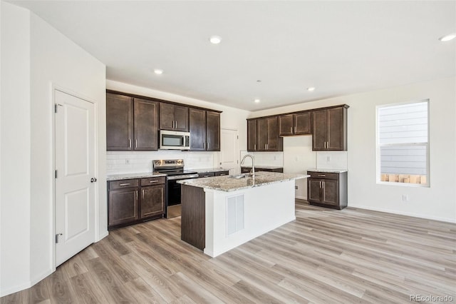 kitchen with stainless steel appliances, sink, a kitchen island with sink, and light hardwood / wood-style floors