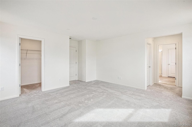 unfurnished bedroom featuring a walk in closet, a closet, and light carpet