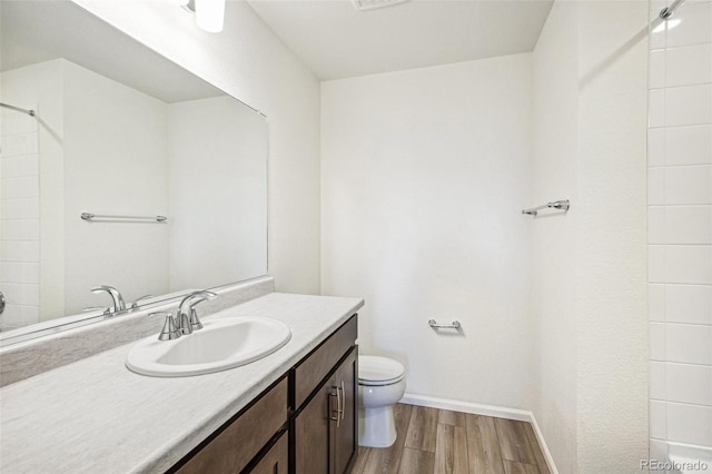 bathroom featuring tiled shower, wood-type flooring, toilet, and vanity