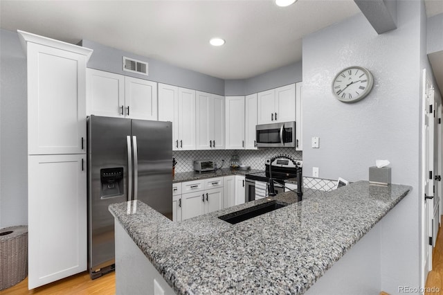 kitchen with appliances with stainless steel finishes, light stone counters, white cabinets, light wood-style floors, and decorative backsplash