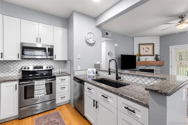kitchen featuring stainless steel appliances, a sink, ceiling fan, dark stone counters, and backsplash