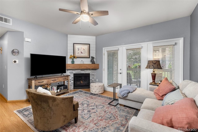 living area with wood finished floors, ceiling fan, a large fireplace, and baseboards