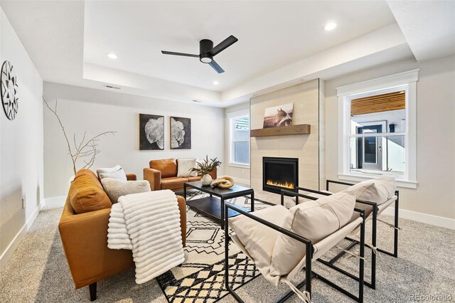 carpeted living room featuring ceiling fan, a tile fireplace, and a tray ceiling