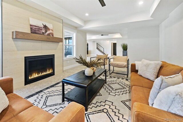 living room with a tiled fireplace, ceiling fan, and carpet