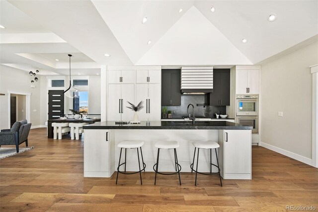 kitchen featuring double oven, a large island with sink, white cabinets, light hardwood / wood-style floors, and lofted ceiling