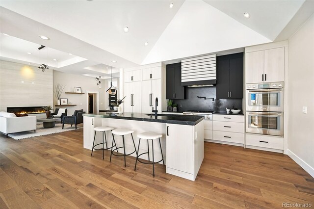 kitchen featuring a large island with sink, white cabinetry, a large fireplace, and light hardwood / wood-style floors