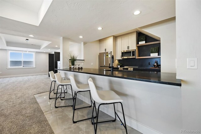 kitchen featuring a breakfast bar, a raised ceiling, sink, appliances with stainless steel finishes, and light colored carpet