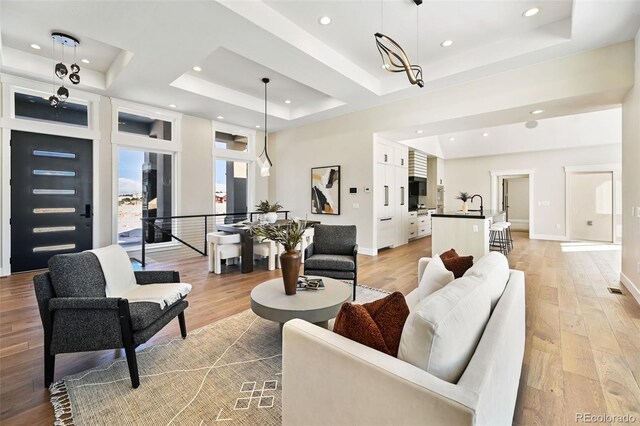 living room with an inviting chandelier, sink, a tray ceiling, and light hardwood / wood-style flooring