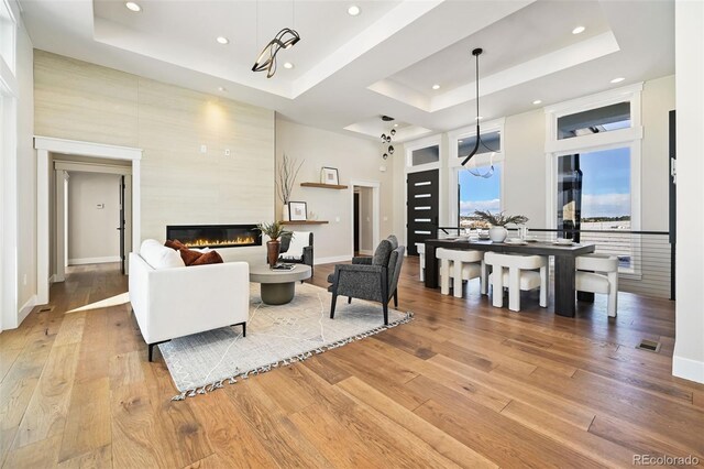 living room featuring a raised ceiling, a towering ceiling, a notable chandelier, and hardwood / wood-style flooring