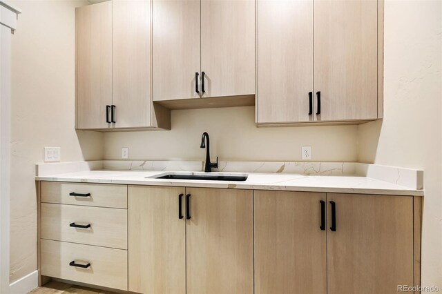 kitchen featuring light stone countertops, sink, and light brown cabinets