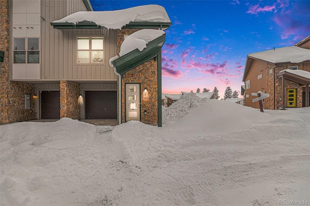 property exterior at dusk featuring stone siding, board and batten siding, and an attached garage