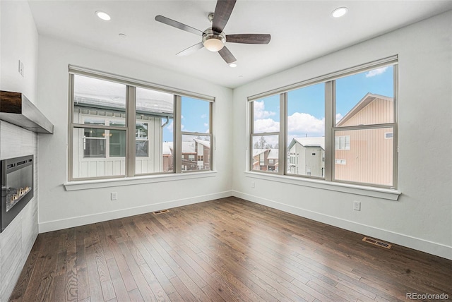 interior space with visible vents, a glass covered fireplace, hardwood / wood-style floors, recessed lighting, and baseboards