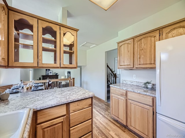 kitchen with light stone countertops, sink, white refrigerator, and light hardwood / wood-style floors