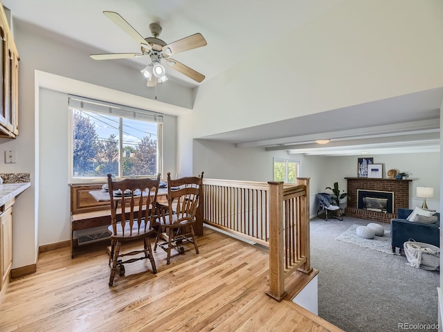 dining area with light wood-type flooring, a brick fireplace, beam ceiling, and ceiling fan