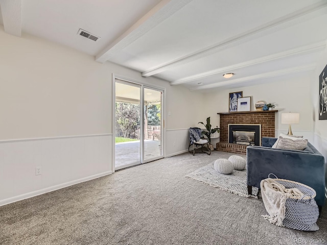 carpeted living room featuring beamed ceiling and a brick fireplace