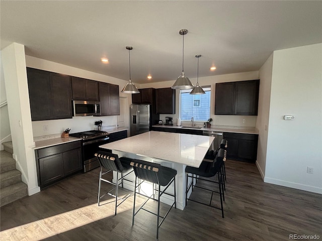 kitchen with sink, a center island, dark hardwood / wood-style floors, decorative light fixtures, and appliances with stainless steel finishes