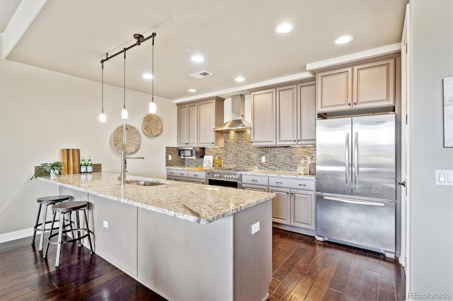 kitchen with wall chimney range hood, hanging light fixtures, stainless steel appliances, light stone counters, and kitchen peninsula