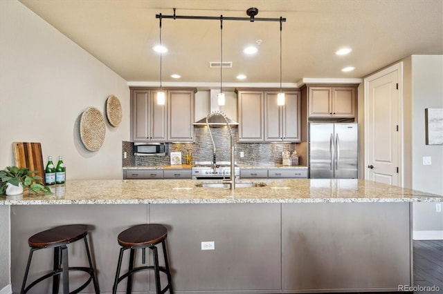 kitchen with pendant lighting, wall chimney range hood, appliances with stainless steel finishes, tasteful backsplash, and light stone countertops