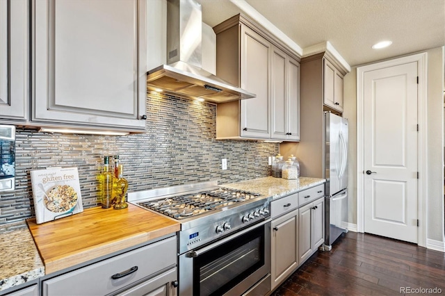 kitchen featuring dark wood-type flooring, gray cabinets, appliances with stainless steel finishes, tasteful backsplash, and wall chimney exhaust hood