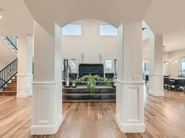 entryway featuring decorative columns, a towering ceiling, and light wood-type flooring