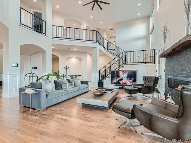 living room featuring a fireplace, light hardwood / wood-style floors, a towering ceiling, and ceiling fan