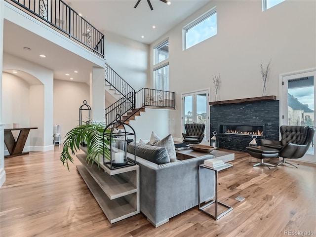 living room with plenty of natural light, light hardwood / wood-style flooring, a stone fireplace, and a towering ceiling