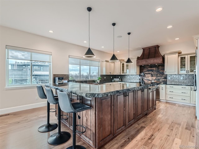 kitchen featuring dark stone countertops, decorative light fixtures, custom range hood, and plenty of natural light