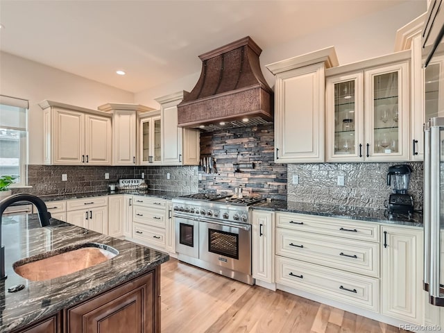 kitchen with sink, range with two ovens, dark stone counters, and custom exhaust hood