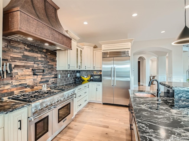 kitchen featuring premium range hood, dark stone countertops, tasteful backsplash, and high quality appliances