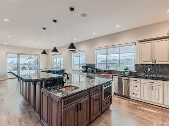 kitchen featuring pendant lighting, dark stone counters, sink, stainless steel dishwasher, and a center island with sink