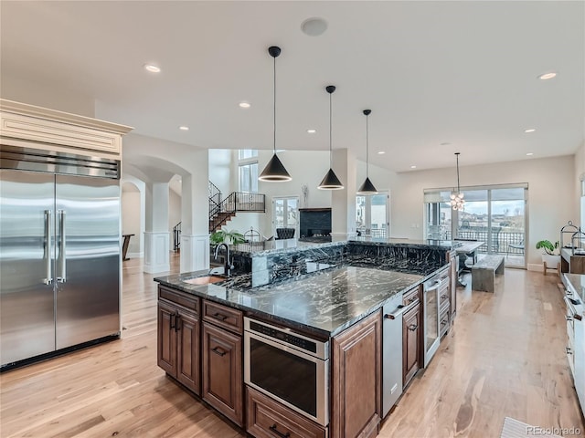 kitchen featuring built in appliances, dark stone counters, pendant lighting, and sink