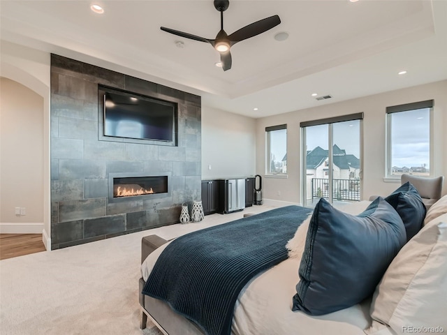 bedroom featuring carpet flooring, a tile fireplace, access to outside, ceiling fan, and a tray ceiling