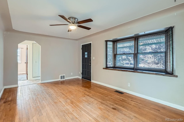 spare room featuring arched walkways, ceiling fan, visible vents, baseboards, and wood-type flooring