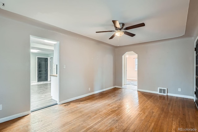 empty room with arched walkways, visible vents, hardwood / wood-style floors, a ceiling fan, and baseboards