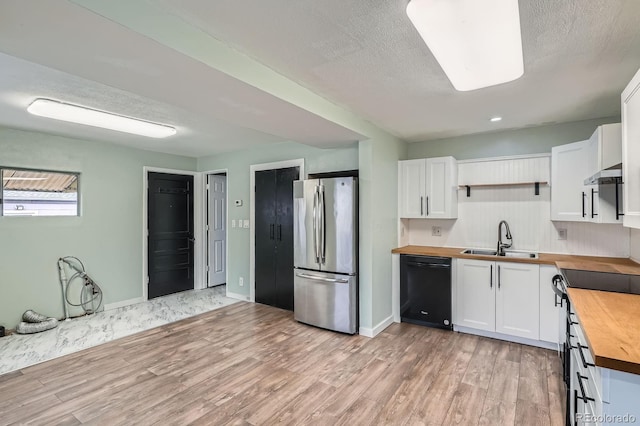 kitchen with butcher block countertops, a sink, white cabinets, freestanding refrigerator, and dishwasher