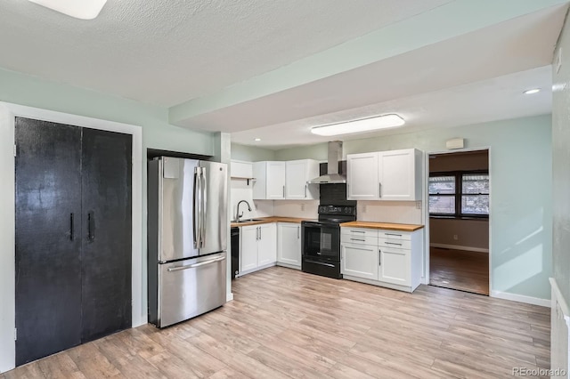 kitchen featuring wooden counters, light wood-style floors, a sink, wall chimney range hood, and black appliances