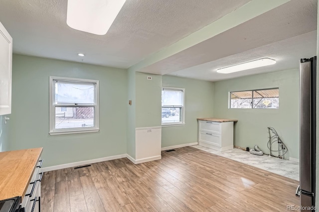 interior space with visible vents, a textured ceiling, baseboards, and wood finished floors