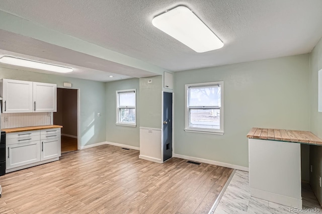 kitchen featuring butcher block countertops, plenty of natural light, white cabinetry, and light wood-style floors