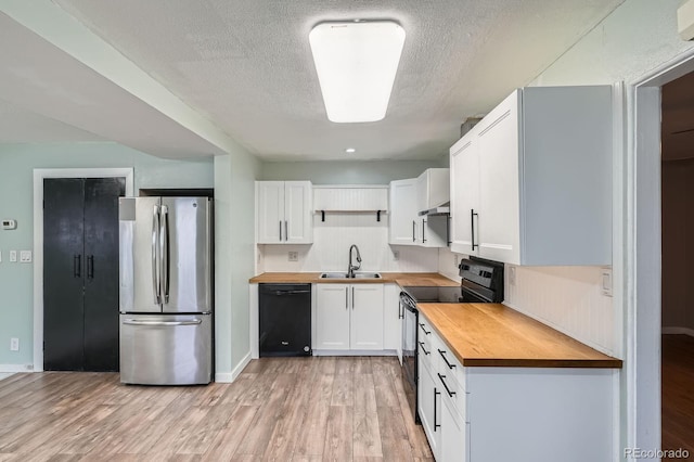 kitchen with a sink, wood counters, white cabinetry, light wood-type flooring, and black appliances