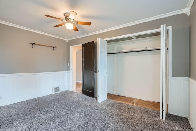 unfurnished bedroom with wainscoting, ceiling fan, crown molding, carpet floors, and a closet