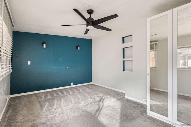 carpeted empty room with a textured ceiling, a ceiling fan, and baseboards