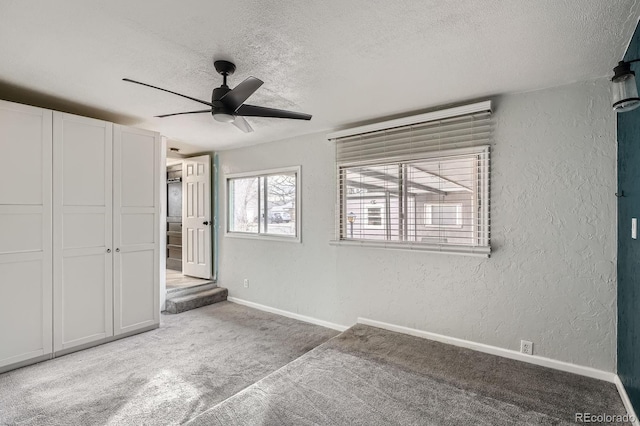 unfurnished bedroom featuring a textured ceiling, a textured wall, a ceiling fan, baseboards, and carpet