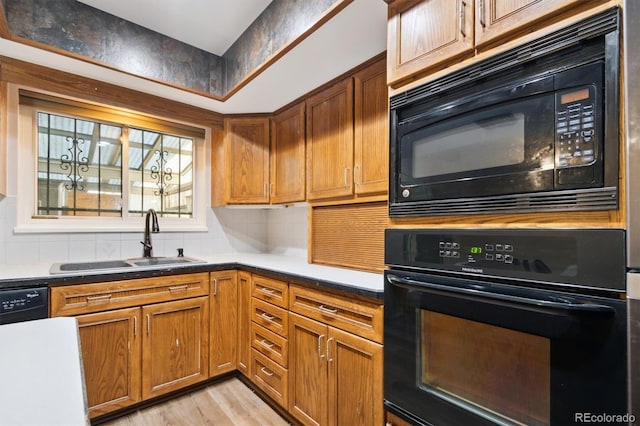 kitchen with light wood finished floors, tasteful backsplash, brown cabinetry, black appliances, and a sink