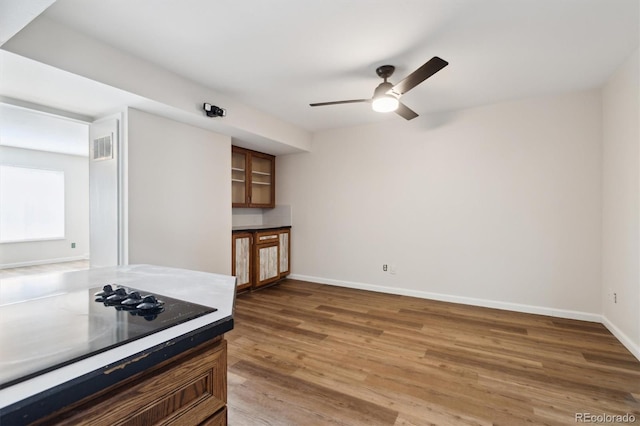 kitchen with ceiling fan, black electric stovetop, wood finished floors, visible vents, and baseboards