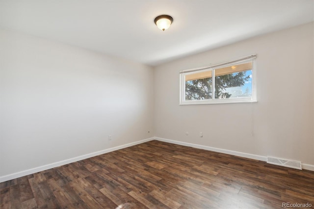 empty room with baseboards, visible vents, and dark wood finished floors