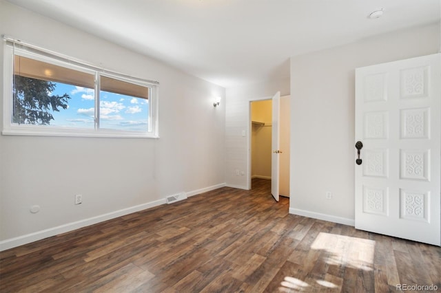 unfurnished bedroom with wood finished floors, visible vents, baseboards, a closet, and a walk in closet